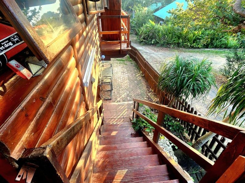 Exterior view of a timber log townhouse featuring a wooden staircase leading down to a brick paved pathway and garden area.