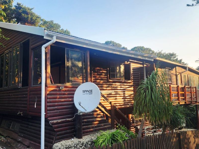 Rear view of a timber log townhouse featuring a raised deck, external staircase, and established garden surroundings.