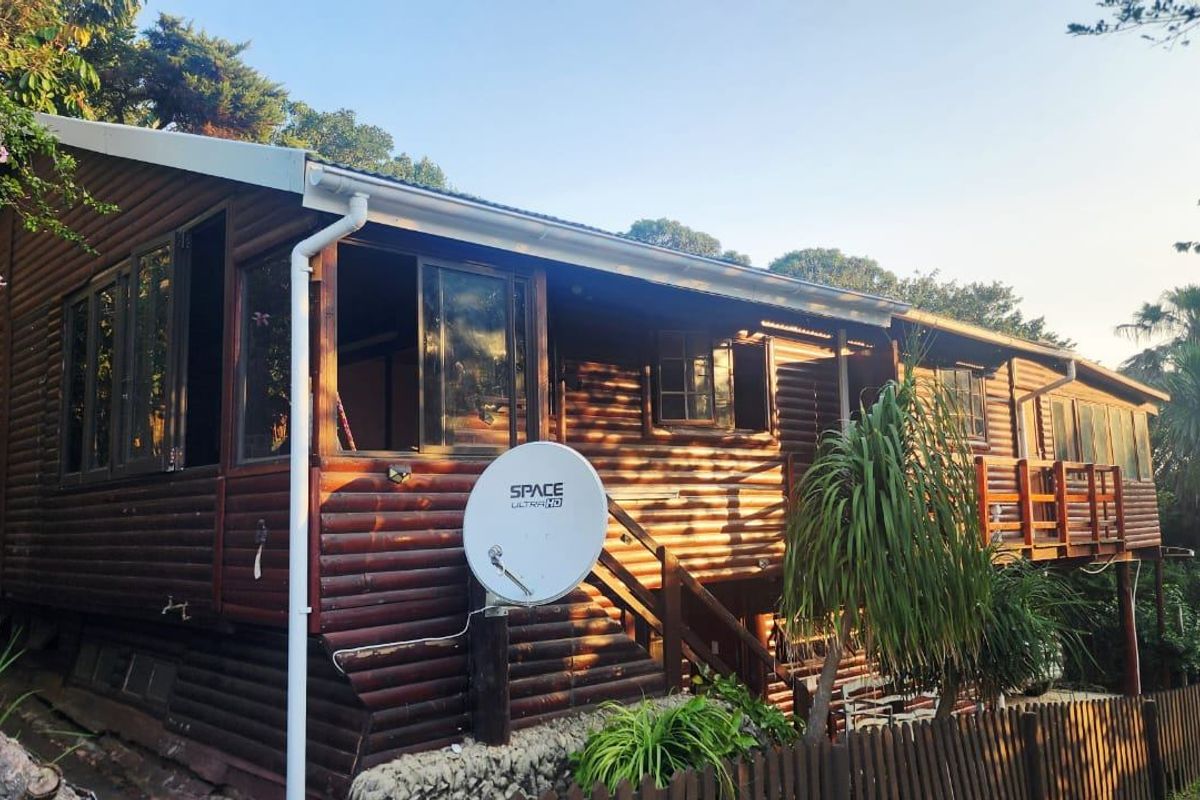 Rear view of a timber log townhouse featuring a raised deck, external staircase, and established garden surroundings.