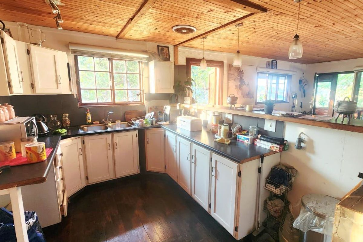 A functional kitchen featuring timber ceilings, white cabinetry, laminate countertops, and a breakfast bar overlooking the adjacent living area.