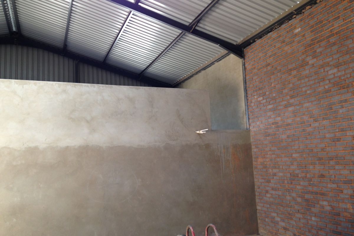 Interior view of an industrial space featuring exposed brickwork, a high corrugated metal roof, and unfinished plastered partition walls.
