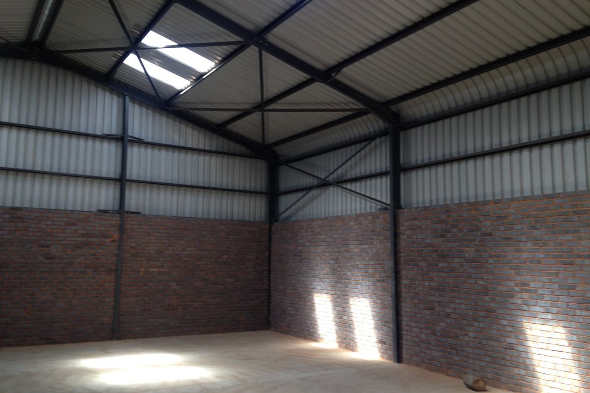 A spacious industrial warehouse unit featuring exposed brick walls, steel structural framing, and a corrugated metal roof with integrated skylights.