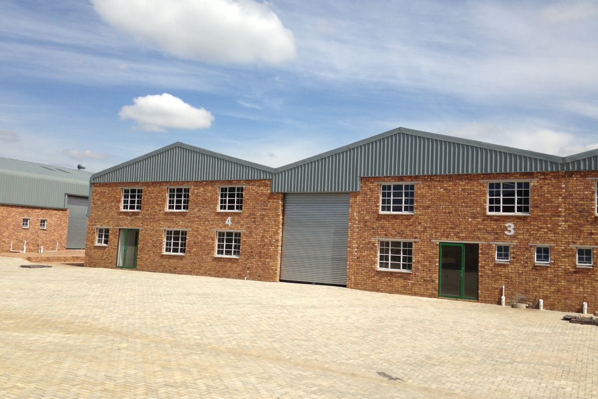 Exterior view of industrial warehouse units featuring face brick facade, metal roofing, and roller shutter doors with paved yard area.