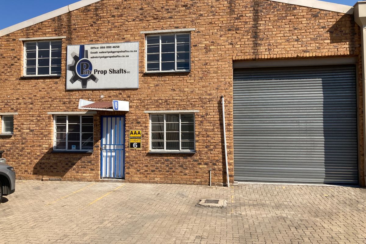 Industrial unit exterior featuring a face-brick facade, large roller shutter door, and dedicated entrance with security gate and paved parking area.