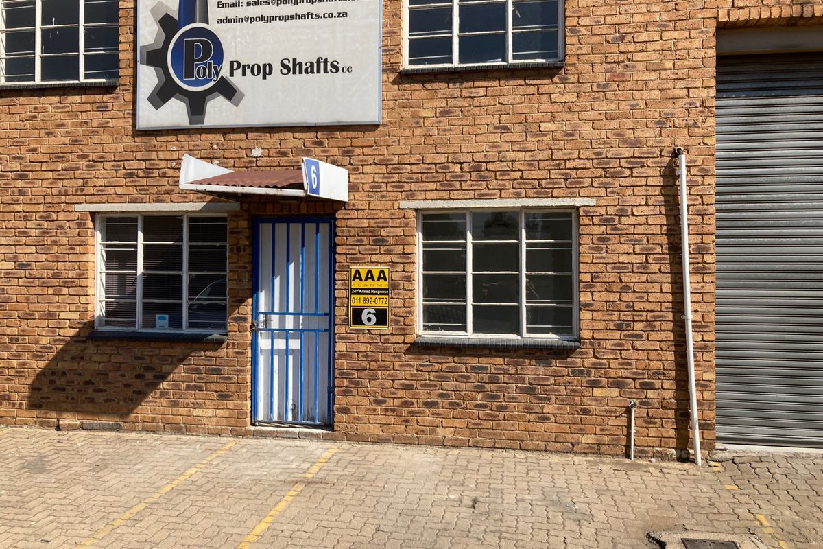 Front exterior view of an industrial unit featuring face brick facade, steel security entrance, and a roller shutter door with dedicated parking space.