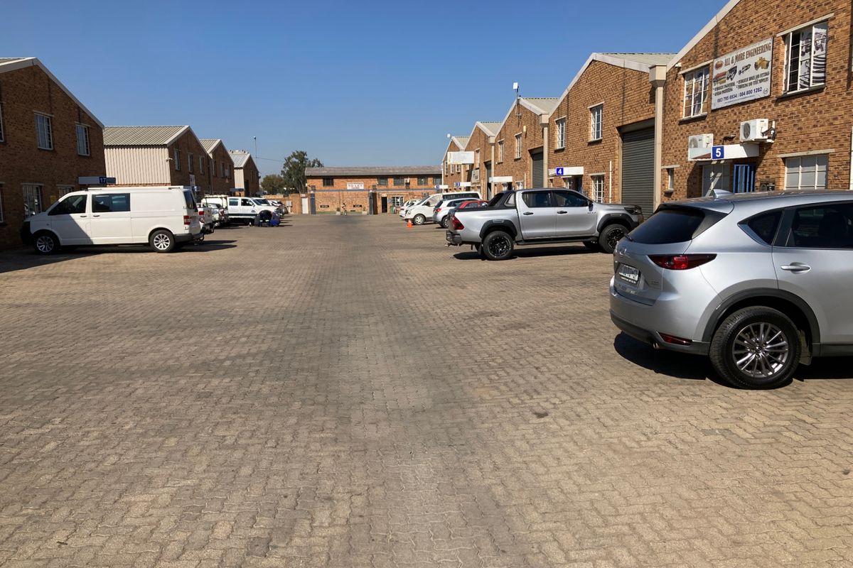 A view of an industrial complex courtyard featuring brick-faced units with roller shutter doors and paved parking area.