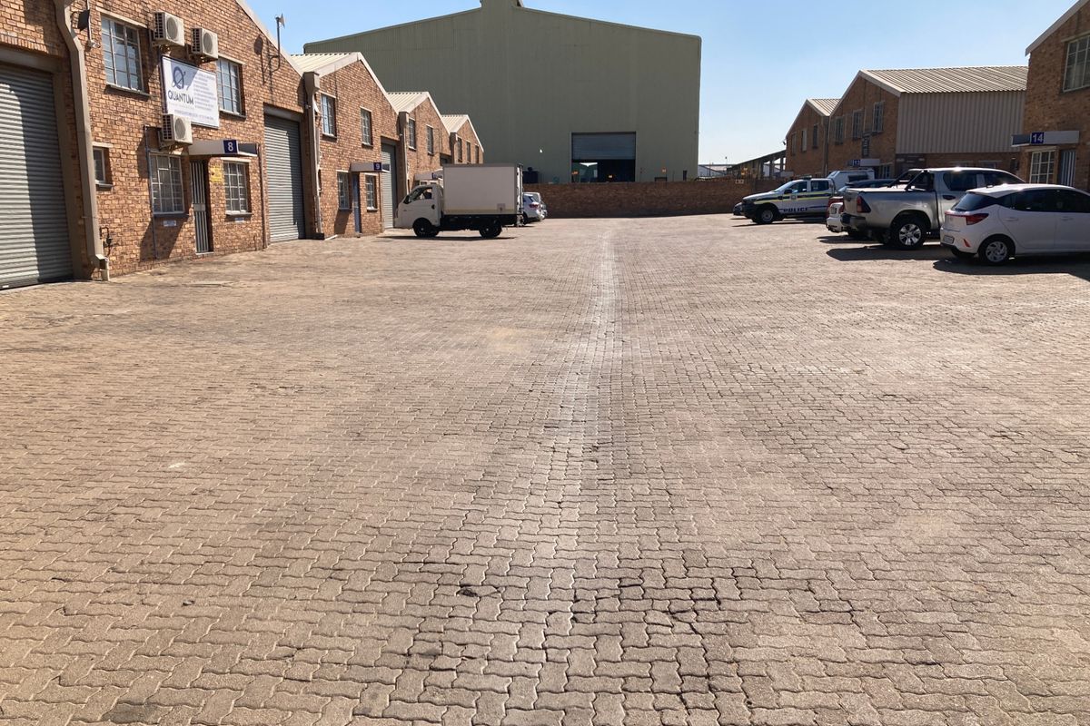 Spacious industrial courtyard featuring paved surfacing, multiple roller shutter access points, and brick-faced warehouse units.