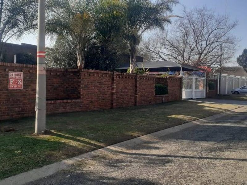 Street view of the property showing the brick boundary wall, security gate, and carport area from the road.