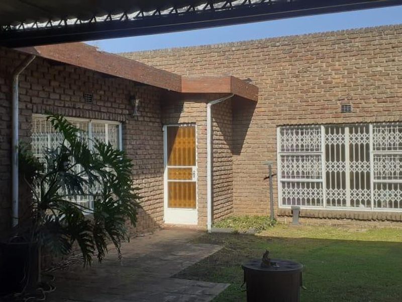 Rear exterior view of the house featuring exposed brick walls, a paved patio area, and security gates on the windows.