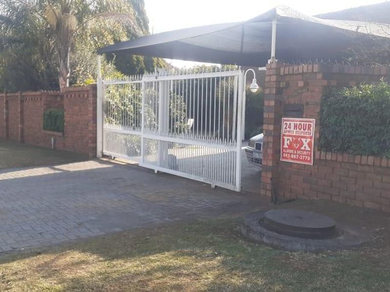 Front exterior view featuring a brick boundary wall, sliding security gate, and a covered carport area.