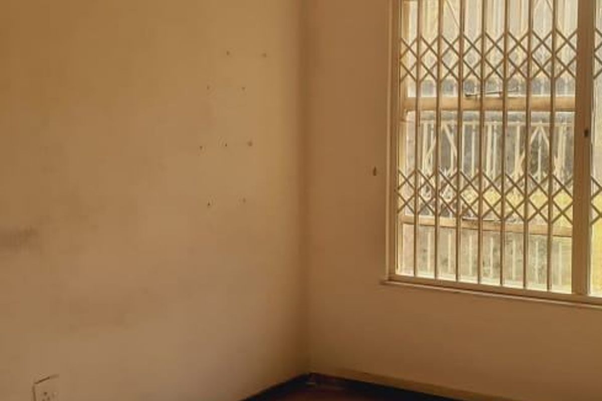 An empty bedroom featuring a ceiling fan and security bars on the window, requiring cosmetic updates to the walls and flooring.