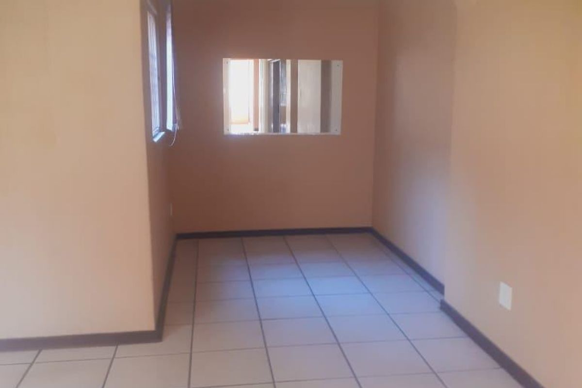 An empty living area featuring neutral wall paint, tiled flooring, and a distinctive arched opening leading to an adjacent space with an internal window.