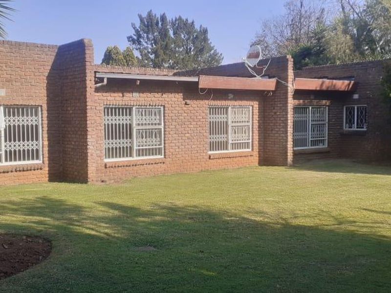 Rear view of a face brick house featuring a spacious lawn, security bars on windows, and satellite dish installation.