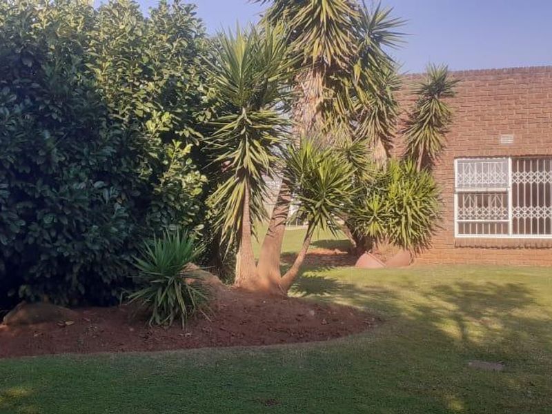 A view of the rear exterior of the house featuring a face brick facade, security-barred windows, and a well-maintained garden area.