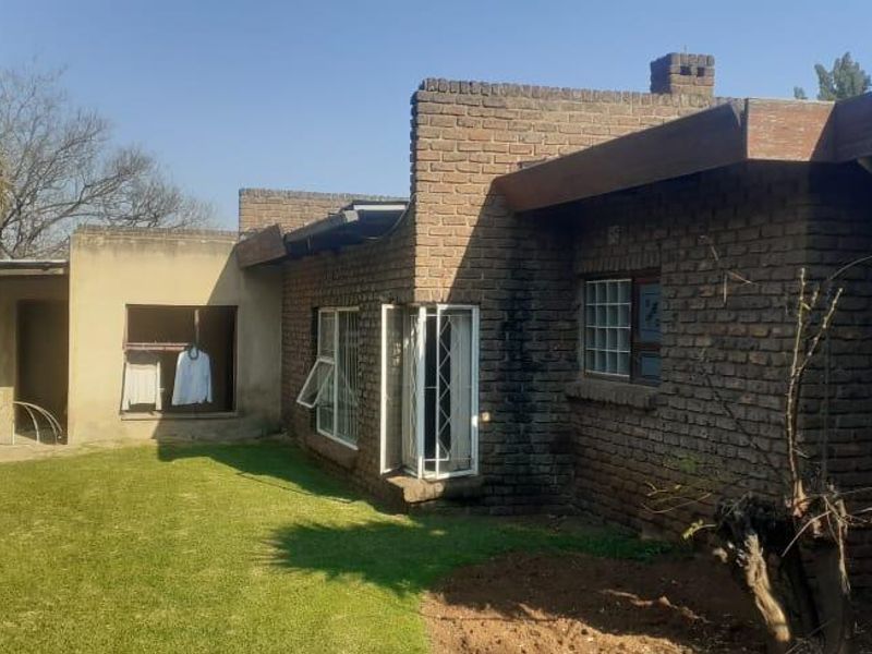 Rear view of a face brick house featuring a small concrete patio, security bars on windows, and a private garden area with boundary walling.