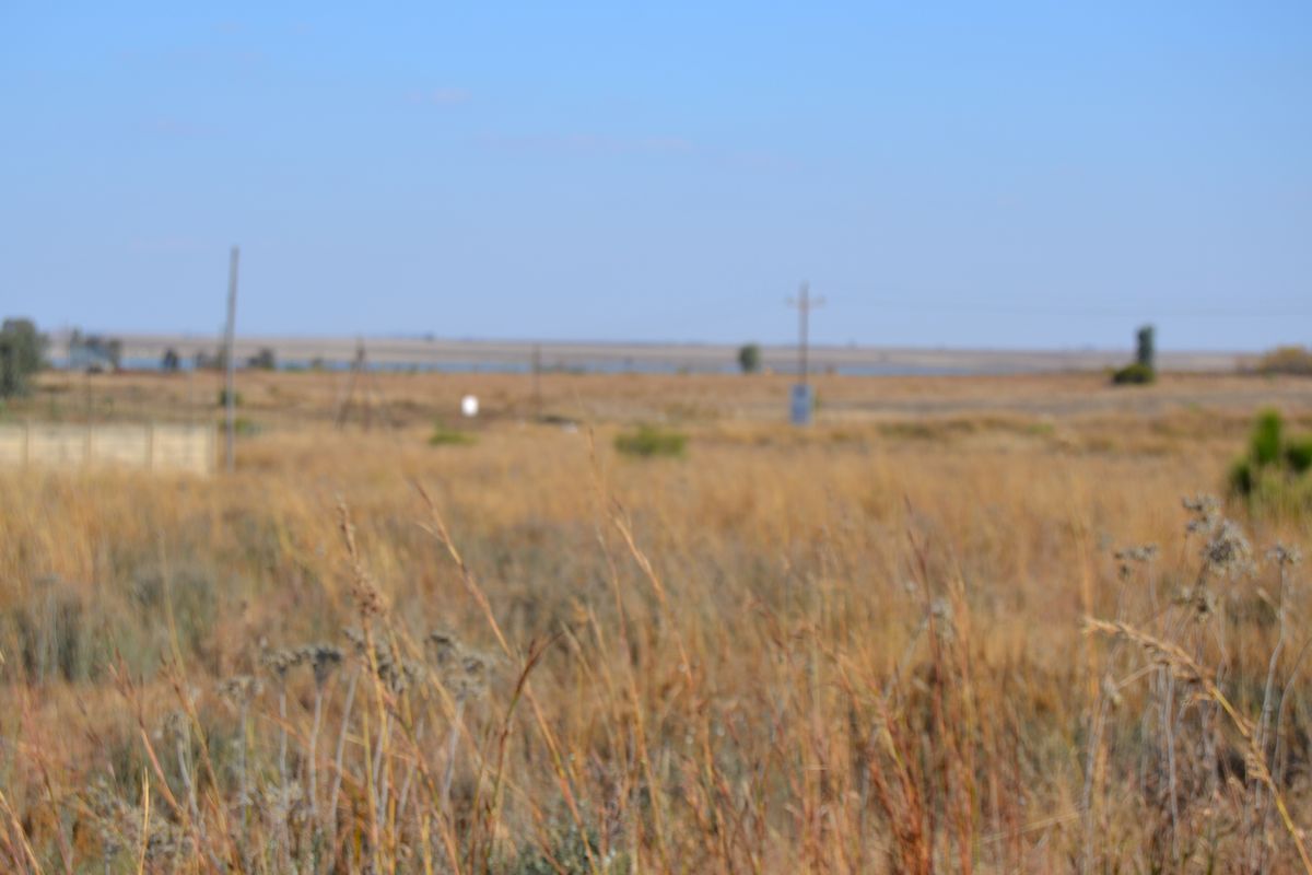 A wide-angle view of the vacant residential land featuring dry grass and distant utility infrastructure under a clear blue sky.