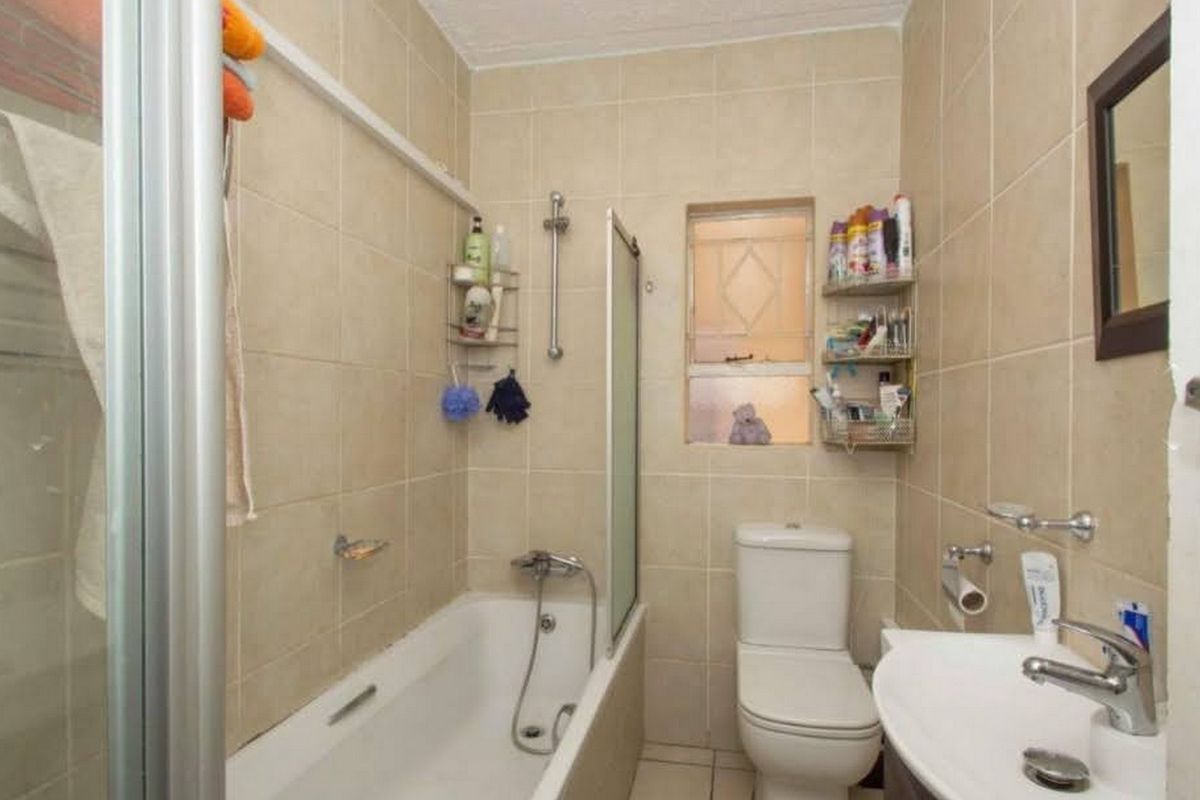 A compact bathroom featuring a bathtub with a shower mixer, a wall-mounted toilet, and a pedestal basin with neutral wall tiling.