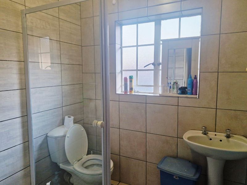 A functional bathroom featuring a pedestal basin, a glass-enclosed shower, and neutral ceramic wall tiling throughout.