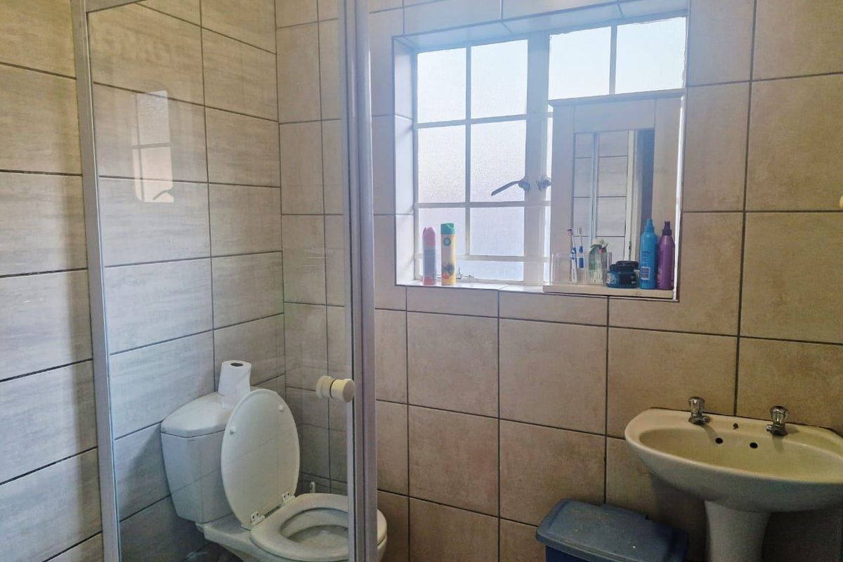 A functional bathroom featuring a pedestal basin, a glass-enclosed shower, and neutral ceramic wall tiling throughout.