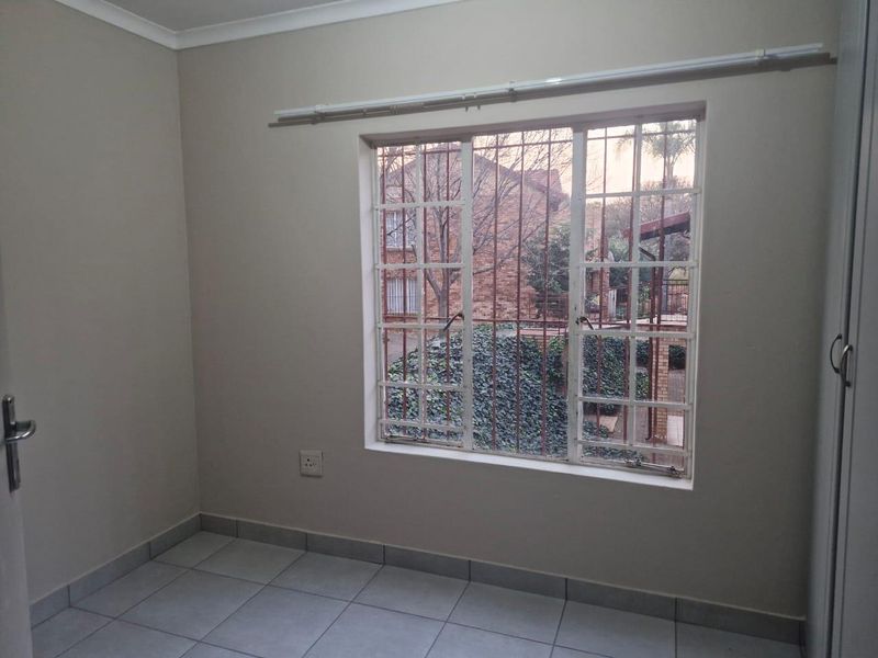 A clean, empty bedroom featuring tiled flooring, a built-in cupboard, and a window fitted with security bars.