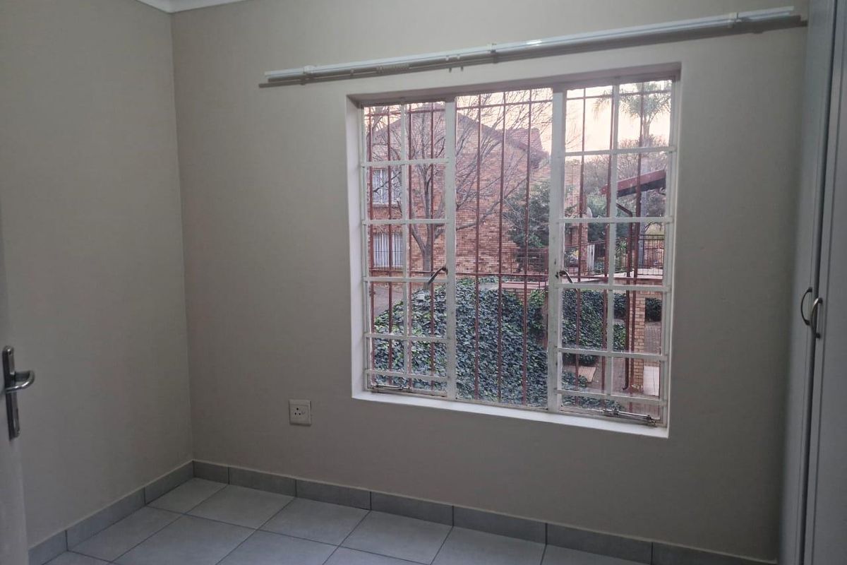 A clean, empty bedroom featuring tiled flooring, a built-in cupboard, and a window fitted with security bars.