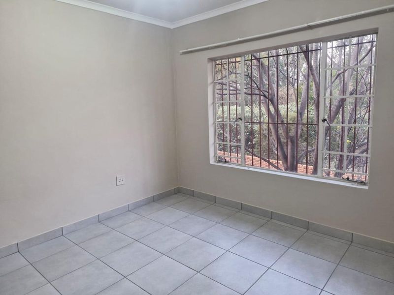 A bright, empty bedroom featuring neutral wall paint, tiled flooring, and a large window fitted with security bars.