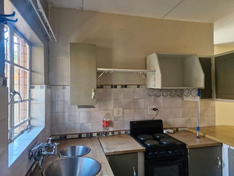 A dated kitchen featuring a double bowl sink, tiled backsplash, laminate countertops, and a freestanding electric stove with overhead storage cabinetry.