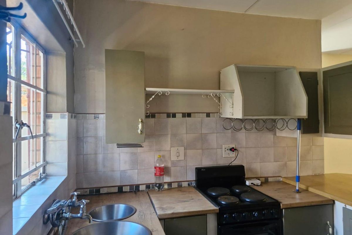 A dated kitchen featuring a double bowl sink, tiled backsplash, laminate countertops, and a freestanding electric stove with overhead storage cabinetry.