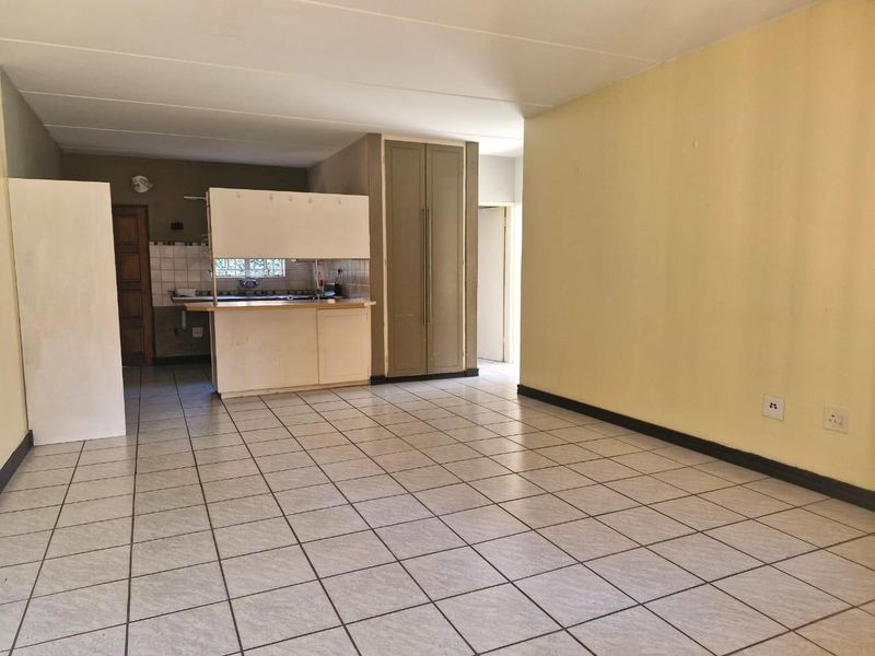An open-plan living and kitchen area featuring tiled flooring, built-in cabinetry, and a breakfast bar, offering a blank canvas for renovation.