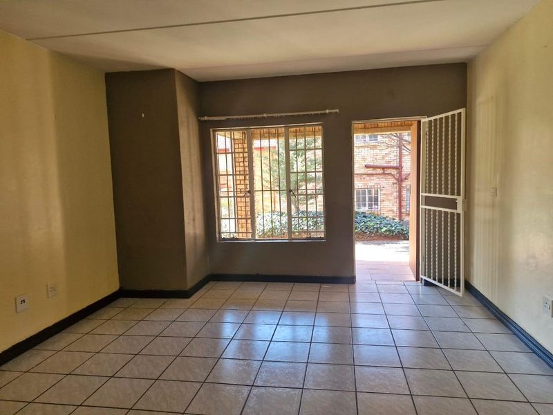 An empty living room featuring tiled flooring, security gate access to the exterior, and burglar bars on the windows.