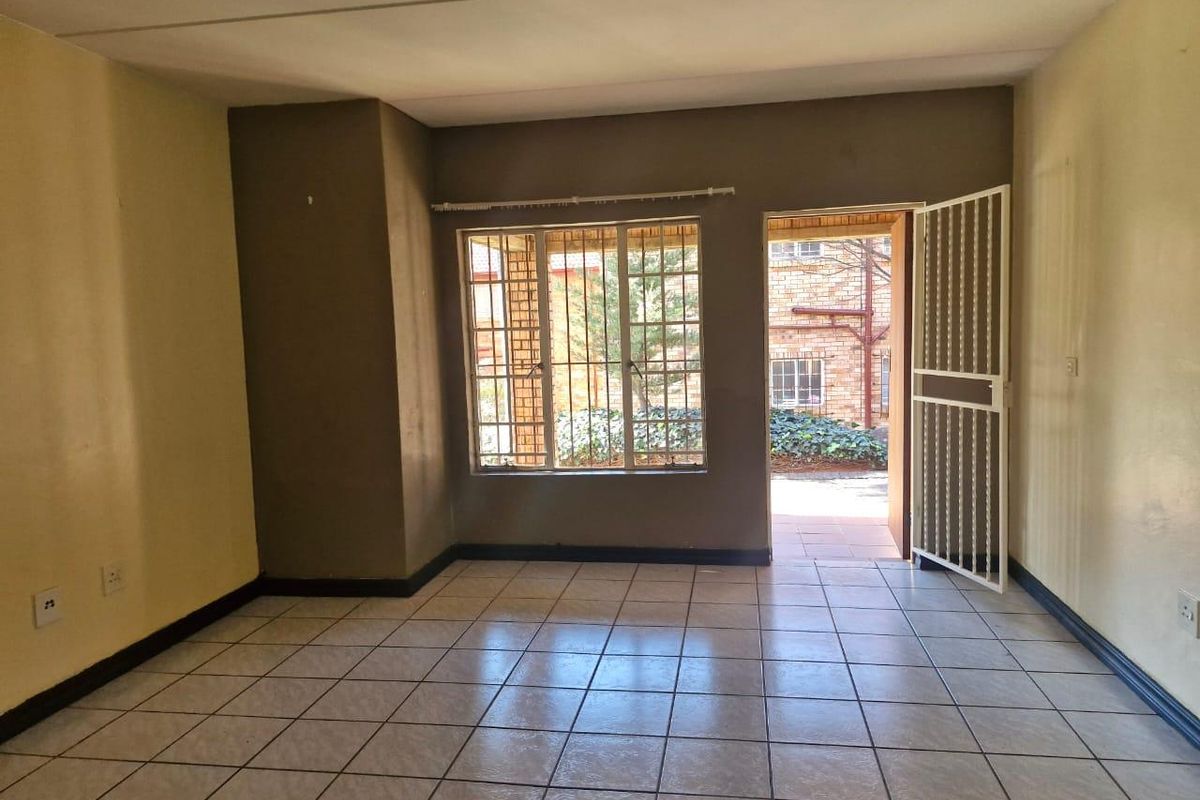 An empty living room featuring tiled flooring, security gate access to the exterior, and burglar bars on the windows.