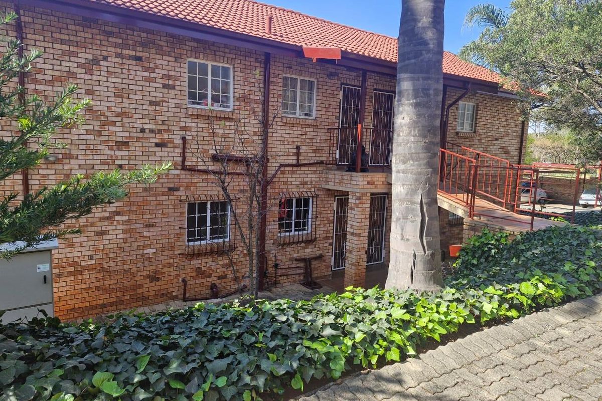Rear view of a multi-story apartment building featuring face brick construction, tiled roofing, and secure access points with metal security gates and bars.