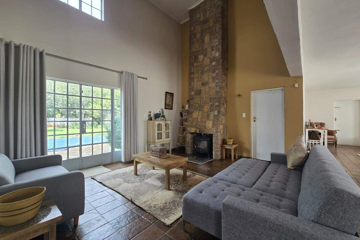 Spacious living room featuring a double-height ceiling, a prominent stone fireplace with a wood-burning stove, and direct access to the pool area via french doors.