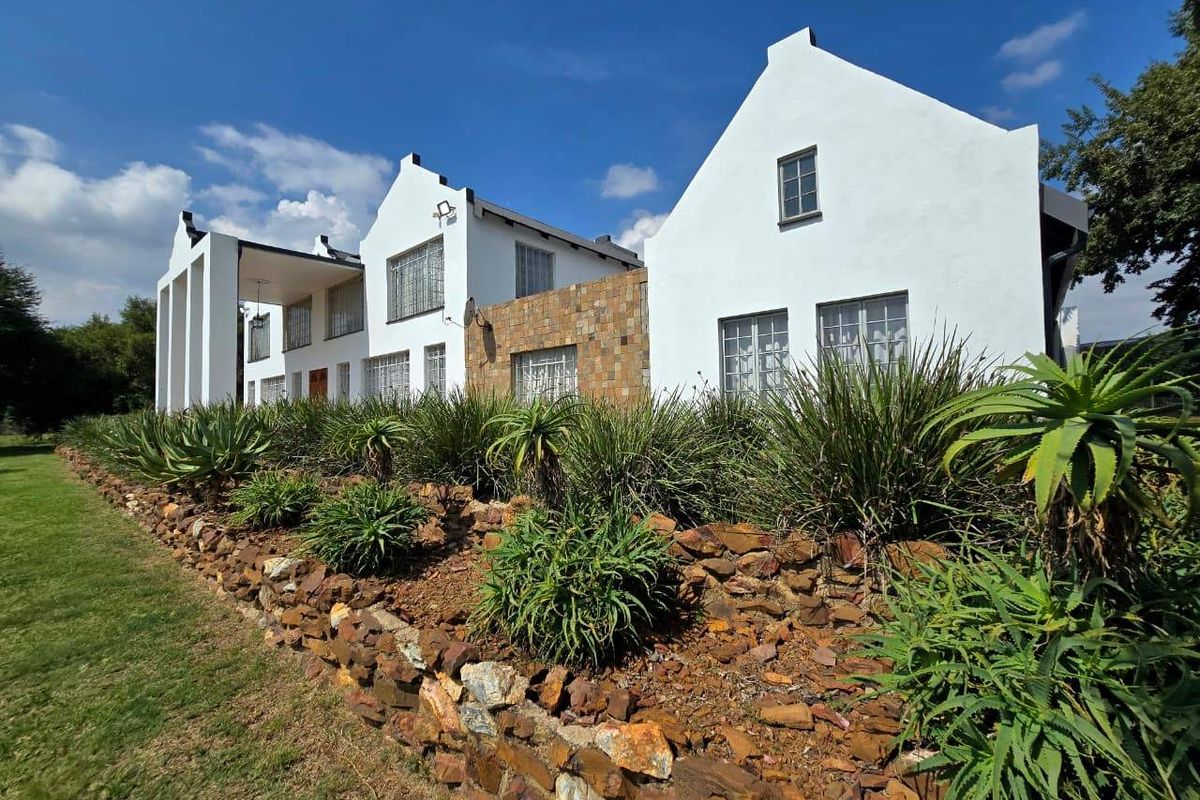 Rear view of a Cape Dutch style house featuring white gabled facades, stone cladding, and a terraced garden with a stone retaining wall.