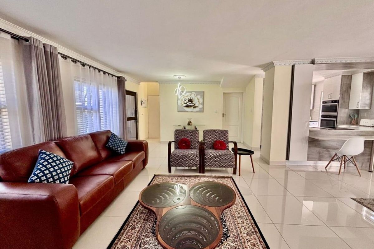 Spacious open-plan living area featuring polished tiled flooring, crown molding, and a modern kitchen with integrated appliances.