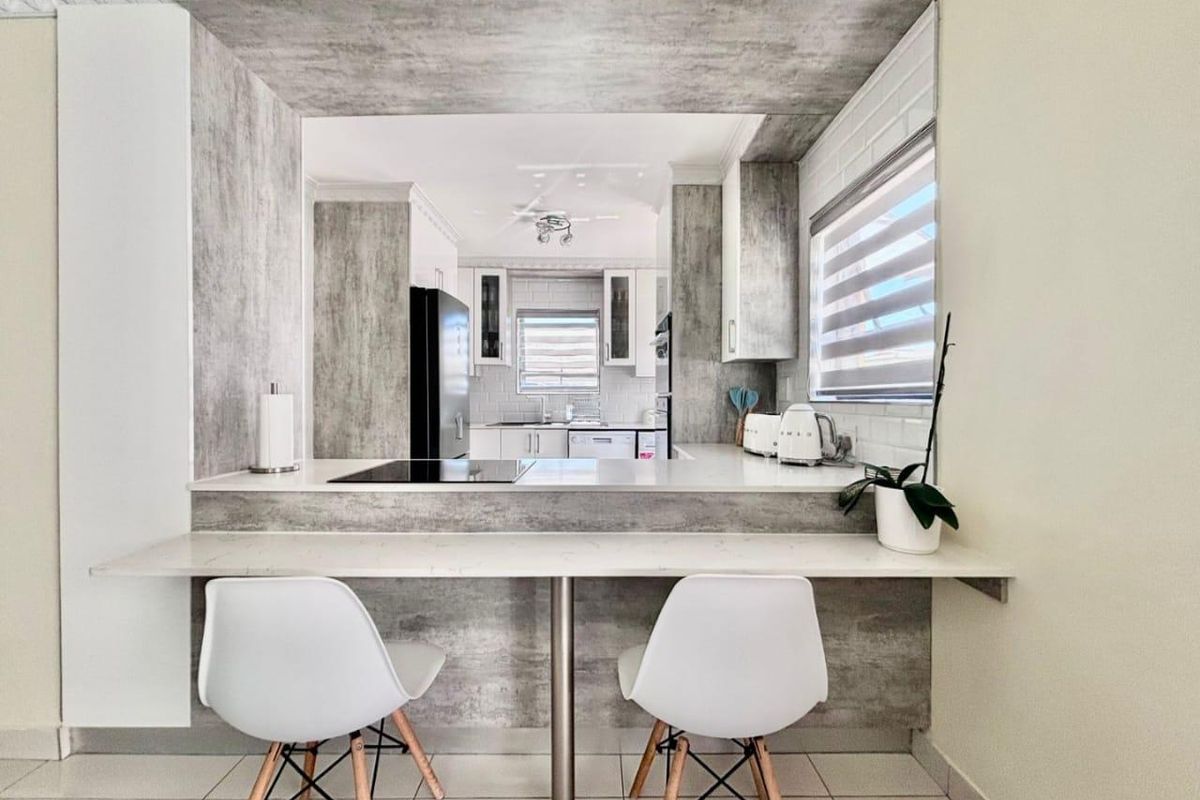 Modern kitchen featuring a breakfast bar, stone countertops, built-in cabinetry, and a sleek electric hob with a subway tile backsplash.