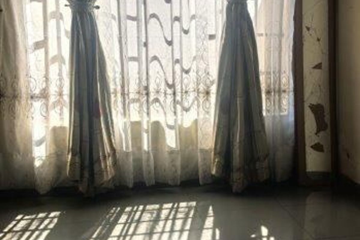 A bedroom featuring tiled flooring and patterned ceiling tiles, with natural light filtering through window curtains.