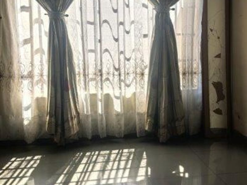 A bedroom featuring tiled flooring and patterned ceiling tiles, with natural light filtering through window curtains.