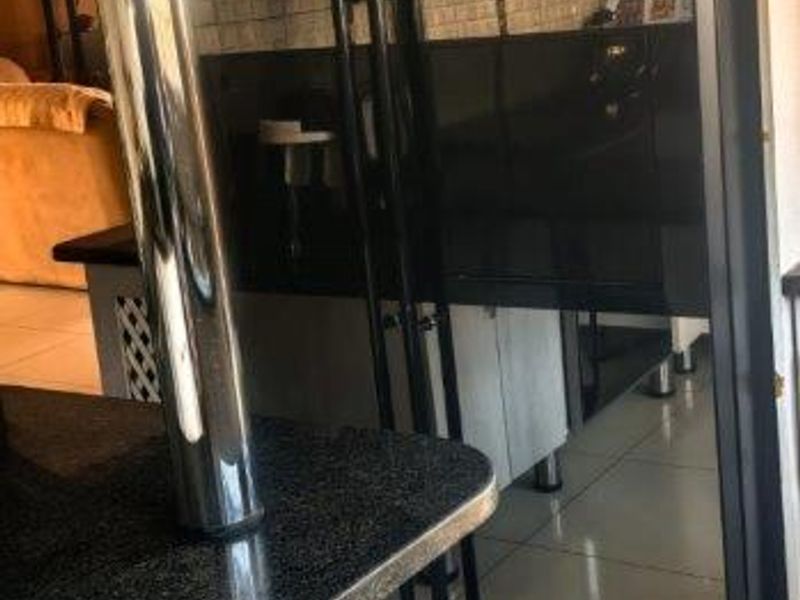 A kitchen area featuring a breakfast bar with a chrome support pillar, tiled flooring, and a tiled splashback.