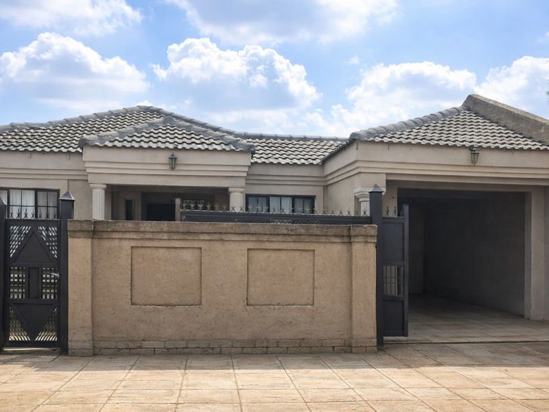 Front elevation of a single-story house featuring a tiled roof, paved driveway, secure boundary wall with metal gate, and a covered garage.