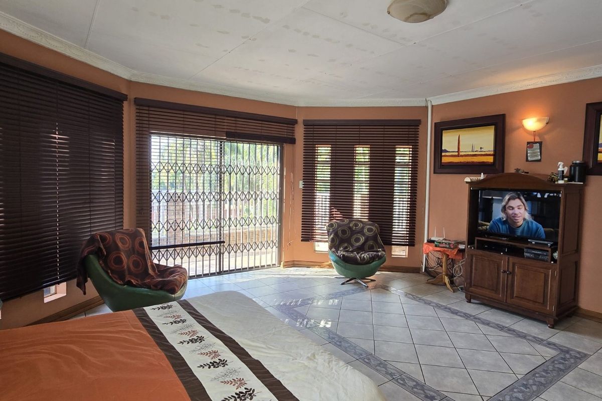 Spacious bedroom featuring tiled flooring, large windows with fitted blinds, and direct access to an outdoor area through sliding security doors.