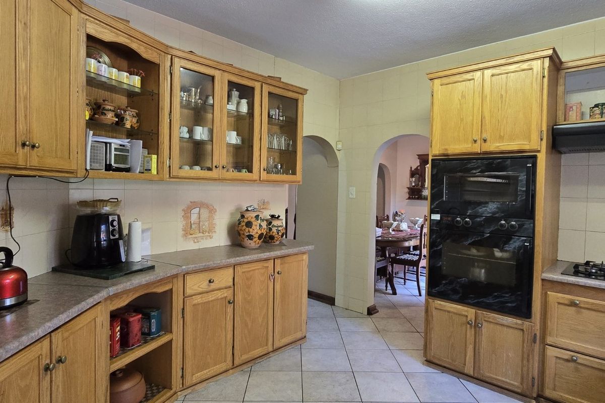 A traditional kitchen featuring oak cabinetry, built-in double oven, gas hob, extractor fan, and tiled flooring with an arched doorway leading to the dining area.
