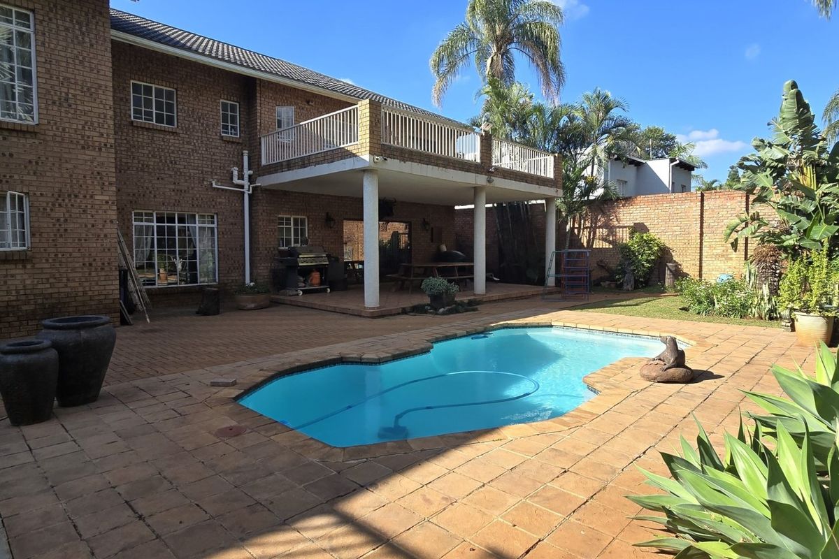 Rear exterior view featuring a swimming pool, paved patio area, and a covered balcony overlooking the garden.