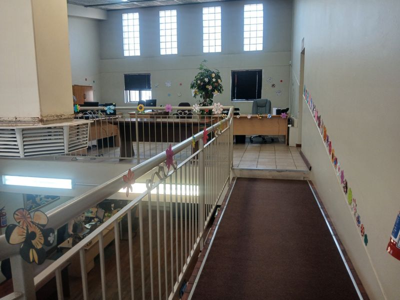 An elevated office mezzanine area featuring a metal balustrade, carpeted walkway, and large glass block windows providing natural light to the workspace below.