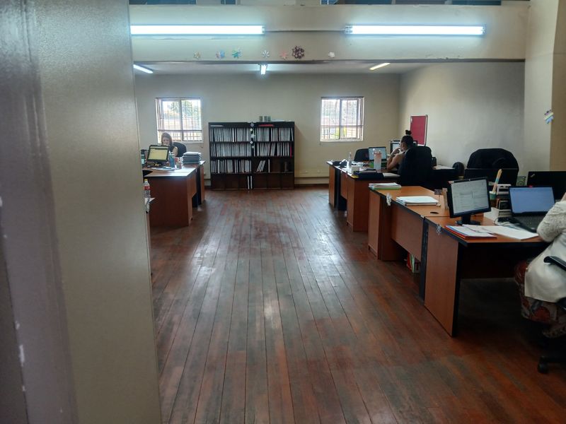 Open-plan commercial office space featuring hardwood flooring, fluorescent lighting, and security-barred windows, providing a functional workspace environment.