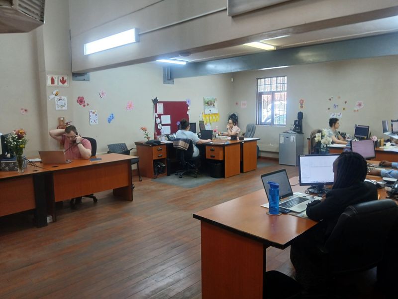 A functional open-plan commercial office space featuring timber flooring, exposed structural beams, and overhead fluorescent lighting, currently configured with multiple workstations.