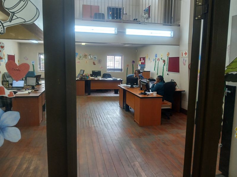 Open-plan office space featuring timber flooring, a mezzanine level with metal balustrade, and fluorescent lighting.