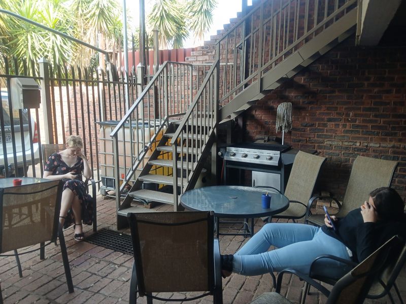 A covered outdoor patio area featuring brick paving, an exposed brick wall, and a metal staircase leading to an upper level.