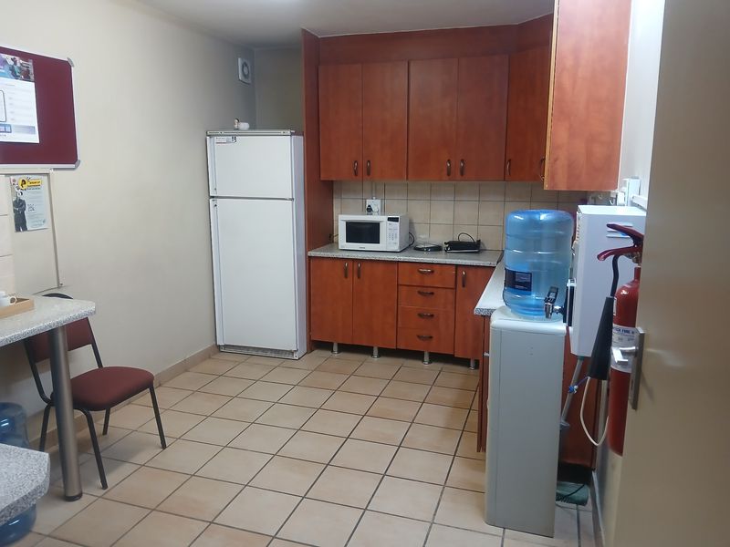 A functional commercial kitchenette featuring wood-look cabinetry, tiled flooring, and a tiled backsplash, providing essential prep and storage space for office staff.