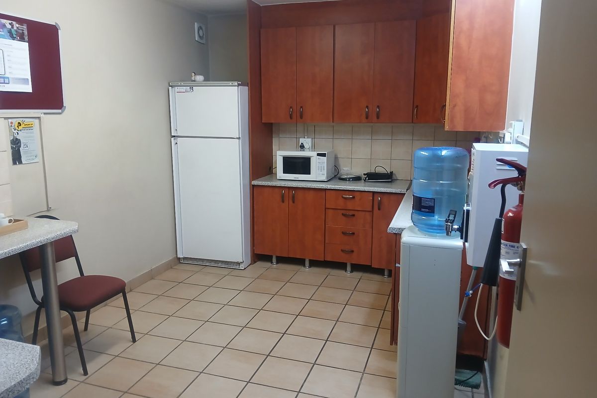 A functional commercial kitchenette featuring wood-look cabinetry, tiled flooring, and a tiled backsplash, providing essential prep and storage space for office staff.
